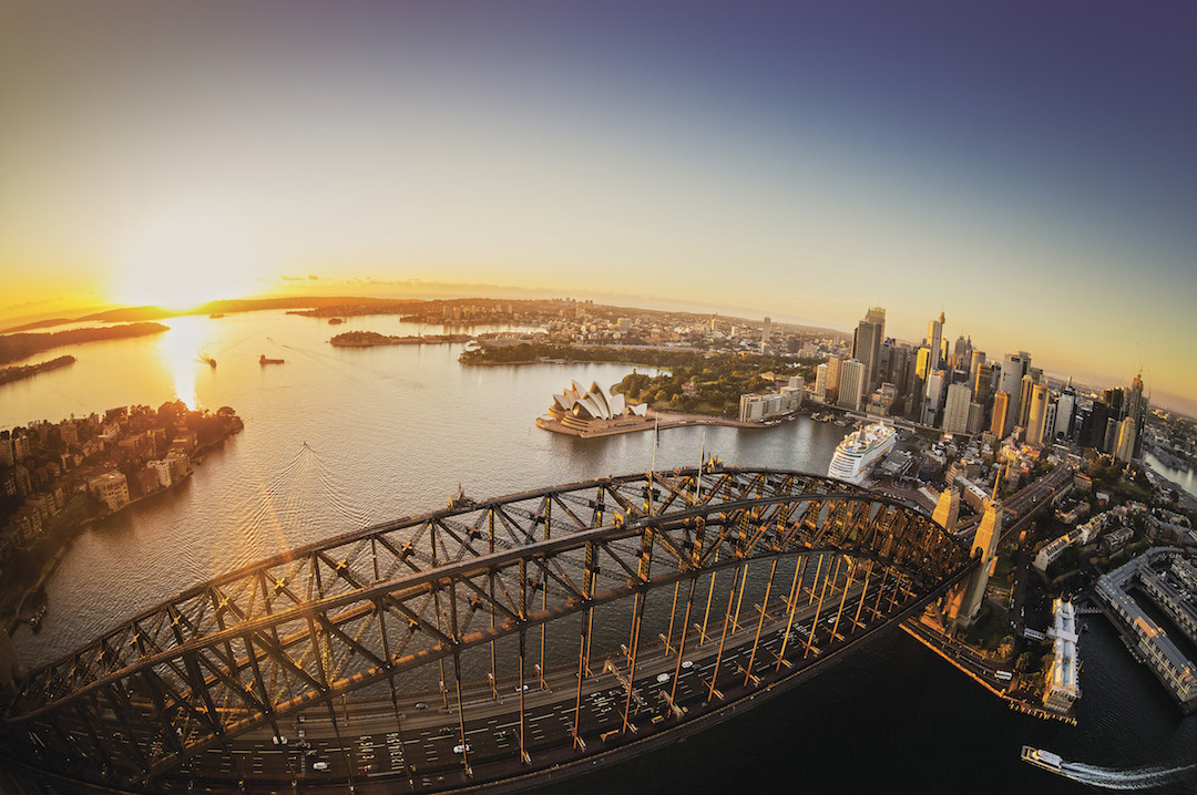 Aerial of the sun rising over Sydney Harbour with views of the Sydney Harbour Bridge and the Sydney Opera House through to the CBD.